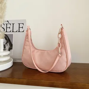 Détail de sac porté épaule en nylon rose avec chaîne en acrylique et tissu lisse.