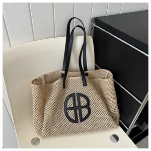 Detailed view of a woven straw beach tote bag with black leather handles and circular logo.
