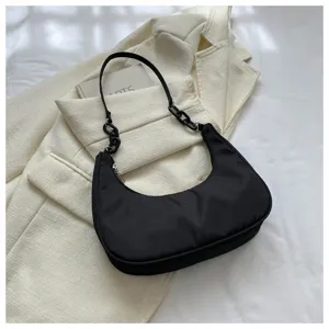 Détail élégant du petit sac à bandoulière hobo en nylon noir sur fond de veste crème.