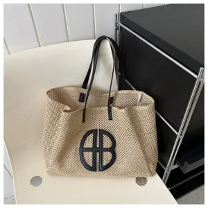 Detailed view of large straw tote bag with black leather handles and stylish round logo.