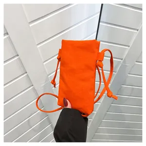Gros plan sur le mini sac bandoulière en toile orange avec sangle fine pour téléphone.