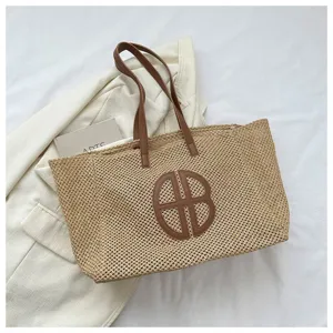 Detailed close-up shot of retro woven straw beach tote bag with brown leather handles and logo.