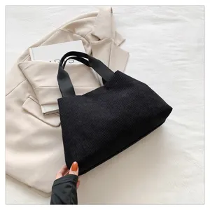 Vue détaillée d'un sac à main en velours côtelé noir avec des anses, sur fond texturé.