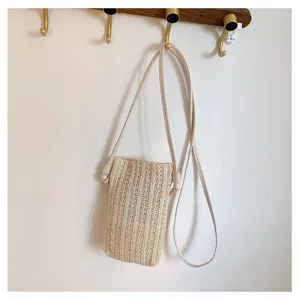 Vue détaillée d'un sac bandoulière chic en paille beige pour téléphone accroché au mur.