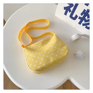 Gedetailleerde opname van een gele nylon schoudertas met witte stippen op een witte tafel.
