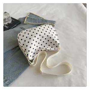Gedetailleerd overzicht van witte nylon schoudertas met zwarte polkadots en verstelbare riem.
