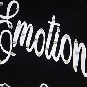 Gros plan sur le détail d'un tissu noir orné de lettres strassées avec le texte emotion.