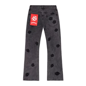 Close-up of black washed denim jeans featuring all-over gothic embroidery and a red tag.