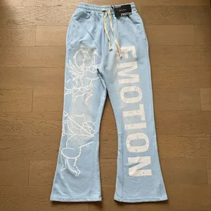 Detail view of light blue streetwear sweatpants with white cupid print and EMOTION text.