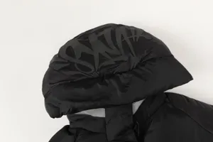Black streetwear puffer jacket detail shot, detachable hood with embossed graffiti logo.