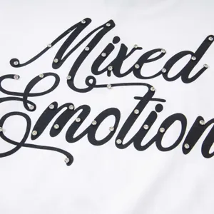 Gros plan détaillé sur un t-shirt blanc avec texte cursif noir et incrustation de strass brillants.