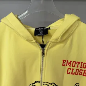 Detailed view of bright yellow zip-up hoodie featuring chest print and brand neck label.