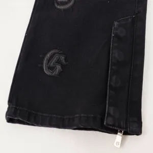 Detail view of black denim jeans cuff with gothic letter embroidery and zipper hem.