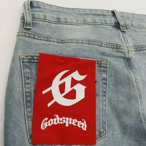 Close-up detail of light blue denim jeans back pocket featuring a red patch with gothic letter.