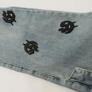 Detailed shot of light wash denim jeans with black gothic letter embroidery design.