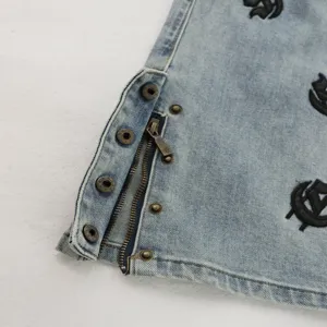 Detailed view of light wash denim pants featuring zipper cuffs and gothic embroidery.