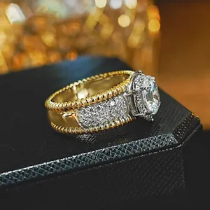Primer plano de anillo bicolor de metal con borde de cuerda diamantes y piedra en caja