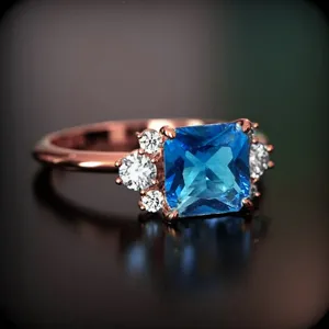 Primer plano de anillo estilo corte gema azul cuadrada con circonitas en oro rosa.