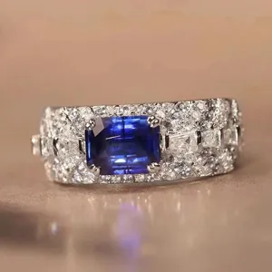 Detailed shot of wide pave diamond ring featuring emerald-cut blue sapphire with double prongs.