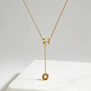 Detailopname van de gouden RVS Y-ketting met strass-cilinderhanger en bungelende kwast.