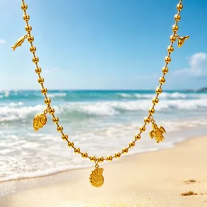 Close-up detail of gold bead necklace with ocean charms like turtle and shell on beach.