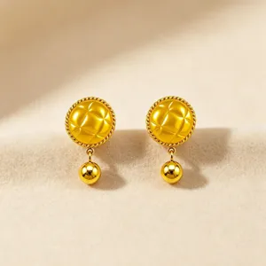 Close-up of golden geometric quilted hanging small ball stud earrings, glossy metal.