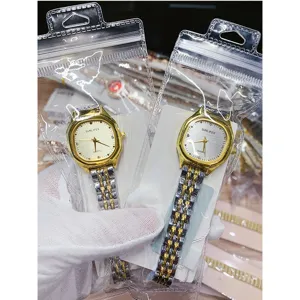 Closeup detail of golden square dial quartz watch with two-tone metal strap in clear packaging.