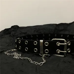 Detail view of a black punk leather belt featuring double grommets and metal chain accent.