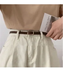 Close-up detail of slim brown leather belt with metal buckle, casual outfit accessory.