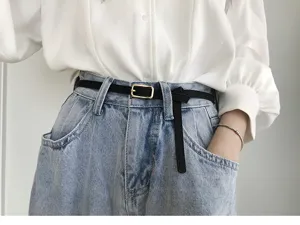 Detail shot of women's thin black belt with gold rectangular buckle for jeans and trousers.