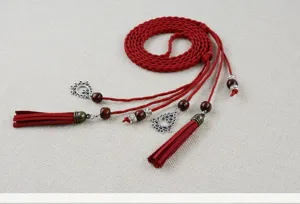 Detail view of red woven waist belt featuring stylish tassels, wood beads, and metal charms.