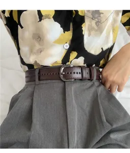 Brown leather punched belt detail shot, paired with grey trousers and floral shirt.