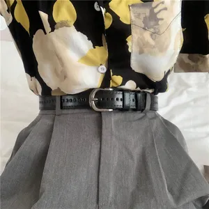 Women's black leather pin buckle belt paired with grey trousers and shirt main view.
