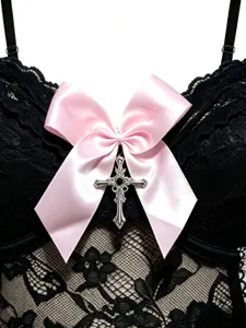 Detail des schwarzen Spitzenkorsetts mit rosa Schleife und glänzendem Metallkreuz.