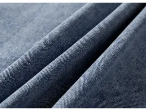 Gros plan de détail sur un tissu en denim bleu, affichant une texture sergée et des drapés doux.
