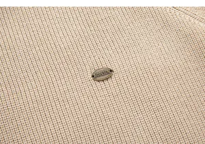 Dettaglio maglione a coste verticali da uomo, tessuto kaki morbido con stemma metallico.