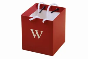 Red square paper gift bag with white letter W and handles, detail view of candy box.