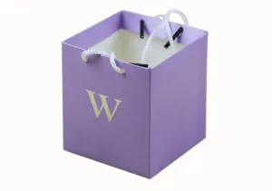 Detail shot of a small purple square paper gift bag featuring white rope handles and letter print.
