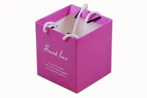 Square pink paper gift bag detail view, sweet candy box packaging with white handles for party.