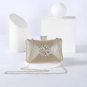Gold glitter evening clutch bag detail with rhinestone flower clasp and gold chain strap.