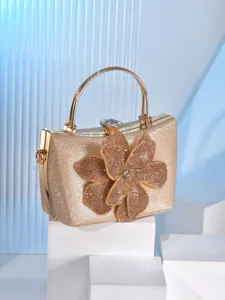 Gold evening clutch bag detail showcasing rhinestone flower decoration and metal handle clasp.