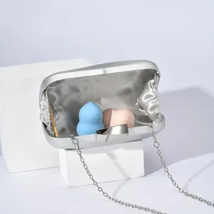 Silver metallic clutch bag detail showing satin lining and chain strap with makeup sponges inside