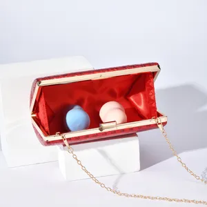 Red evening clutch bag detail showing gold tone metal lock, chain strap and red interior.
