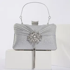 Détail de pochette de soirée argentée avec broche florale strassée et pendentif gland.