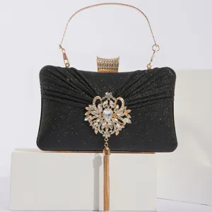 Élégante pochette de soirée noire pailletée, poignée dorée et broche florale en strass.