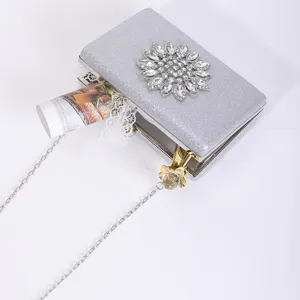 Silver glitter evening clutch bag detail, sparkling rhinestone flower brooch and chain strap.