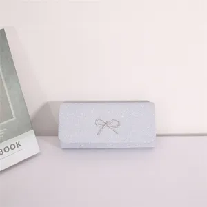 Silver glitter evening clutch bag with sparkling rhinestone bow detail closeup view.