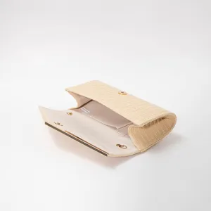 Detailed view of beige straw envelope clutch bag with gold tone metal trim and interior pocket.