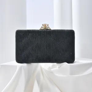 Close-up details of the black evening clutch with crystal clasp, showing textured fabric.