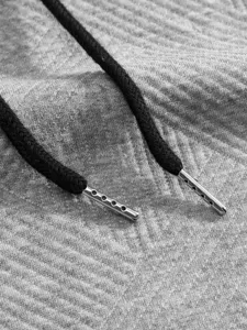 Détail de sweat à capuche en tissu jacquard gris avec cordon noir et embout métal.